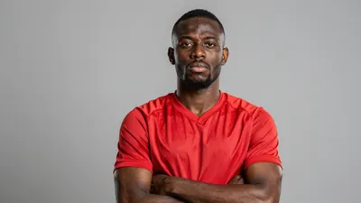 Photorealistic portrait of a muscular 27-year-old African male footballer, wearing a solid red jersey with smooth fabric...