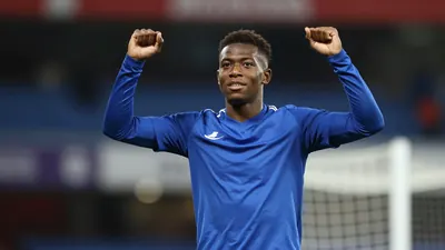 Photorealistic portrait of a 17-year-old African male footballer in a solid blue training kit, waist-up shot, celebrating...